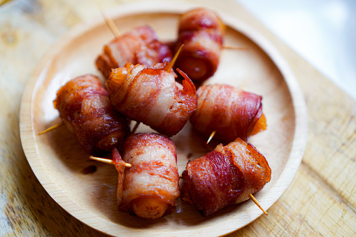 A close-up photo shows skewers of Bacon Wrapped Sausage lined up on a ready-to-eat plate.