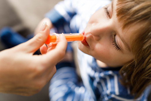 Close up of unrecognizable parent giving little boy a medical syrup from a syringe.
