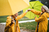 Happy mature couple in yellow raincoats having fun on rain in nature.