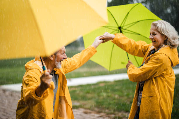 happy mature couple in yellow raincoats having fun on rain in nature. - umbrella senior adult couple autumn imagens e fotografias de stock