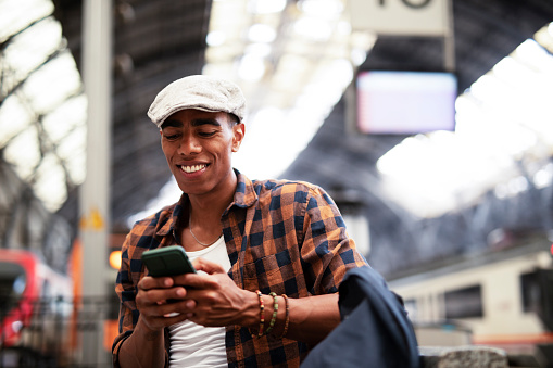Happy young man waiting for the train. African man waiting in a subway. Man using the phone