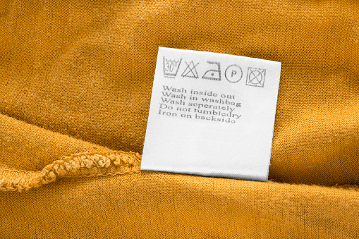 Washing instructions clothing label on yellow fabric closeup