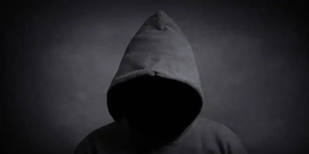 faceless person wearing black hoodie hiding face in shadow - mystery crime conspiracy concept
