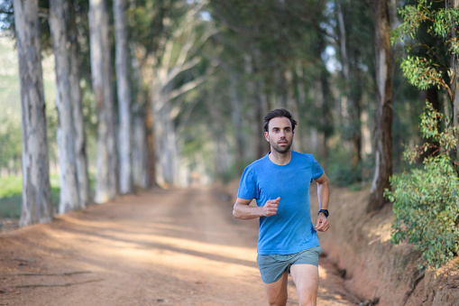 Male mid adult fit strong runner running together on a gravel road in a eucalyptus forest, Stellenbosch, South Africa.