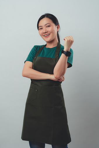 Asian woman wearing apron happy smiling and looking at camera, standing isolated on background.