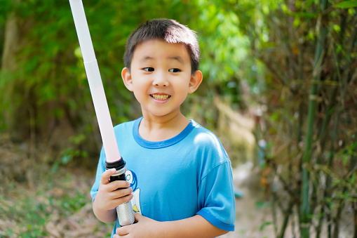 The picture shows a boy smiling happily as he plays a lightsaber duel with his brother.