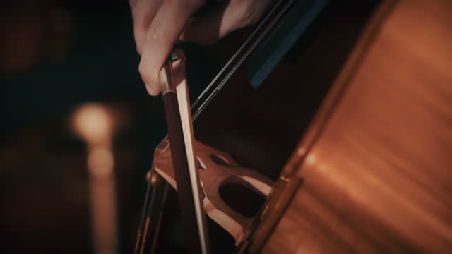 Closeup video of a cellist playing strings with bow on a dark background