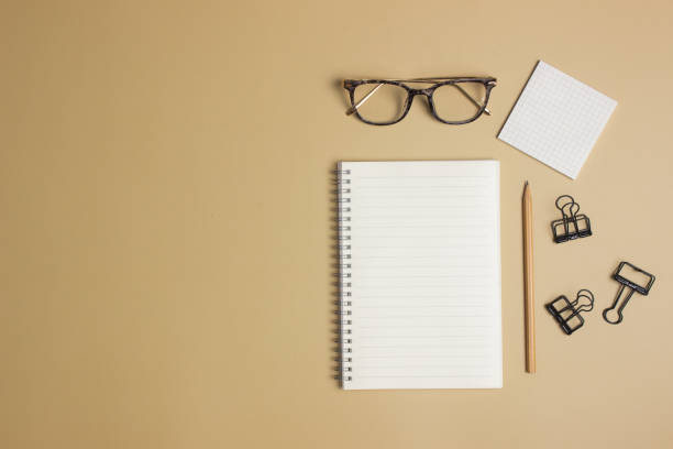 istock White notebook with glasses, pencil and black clip over the brown background. 1487451511