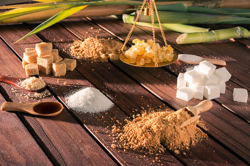 different types of sugar on a wooden table, a scale with sugar beads and sugar canes in the background