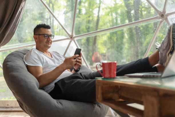 istock Man Sitting In Geo Dome Glamping Tent And Using Smartphone. 1487453708