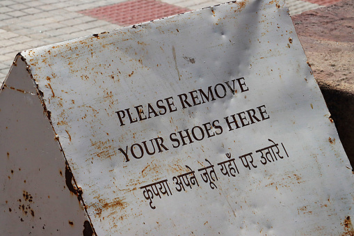 Stock photo showing close-up view of rusty, metal sign requesting the removal of footwear.