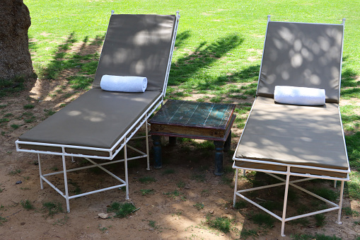 Stock photo showing close-up view of pair of fake leather cushioned, metal sun lounger beds in shade on sunny, lawn.