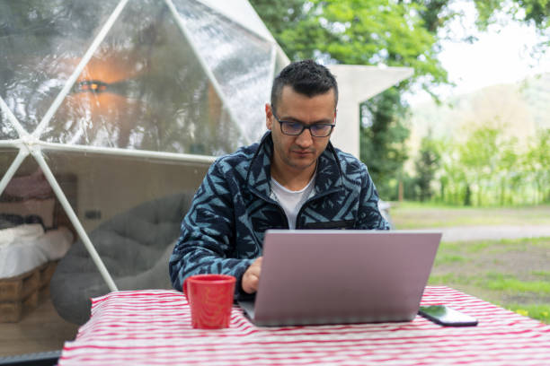 istock Man Sitting At Table And Using Laptop In Front Of A Geo Dome Glamping Tent. 1487455048