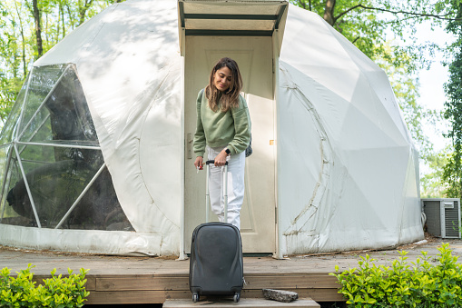 Woman Entering Glamping Tent Hotel In The Forest With Her Suitcase.