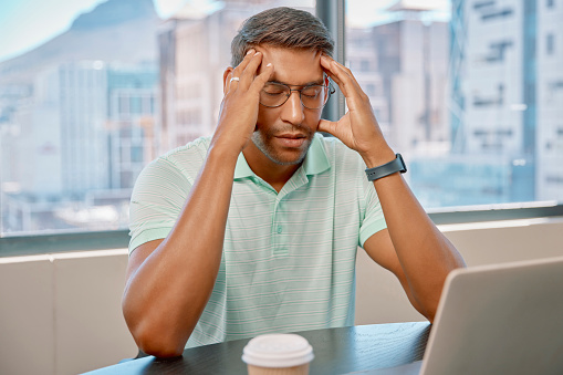 Stress, headache and man in the office while working on company project with a laptop. Technology, burnout and professional male employee with tired migraine doing research with computer in workplace