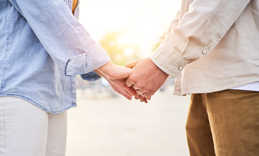 Beautiful close up photo of two unrecognisable people holding hands outside. Young in love caucasian couple getting engaged during sunset. Copy space image.