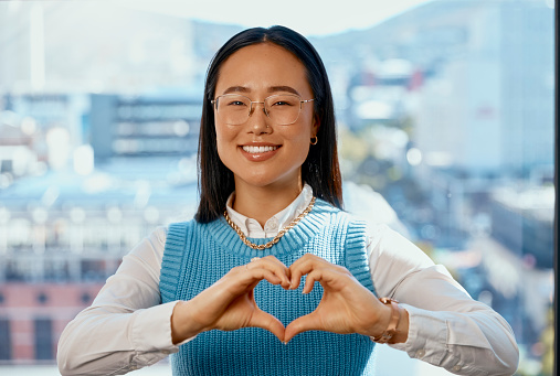 Portrait, smile and business woman with heart hands for affection, care and romance in office. Love, hand gesture and Asian professional with emoji for kindness, commitment or empathy in workplace.