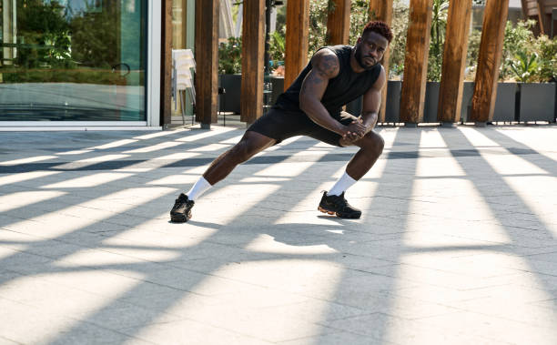 Fit sporty young black man doing warm up exercises in workout park.