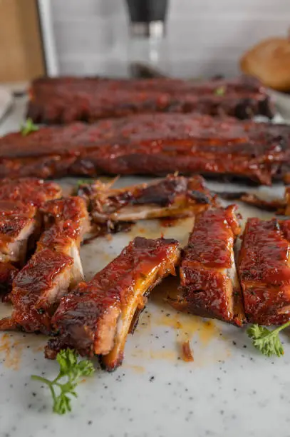 Homemade fresh barbecue pork ribs with honey, barbecue sauce glaze. Served hot and slice on a cutting board with whole ribs in the background. Closeup, front view