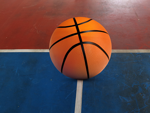 A basketball is placed on the red and green surface of the basketball court.