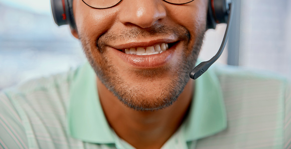 Closeup of a mouth of a man call center agent doing an online consultation with a headset in the office. Happy, smile and male customer service representative working on a crm strategy in workplace.
