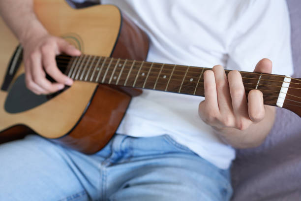 istock Young man playing acoustic guitar on sofa at home, closeup view 1487463593
