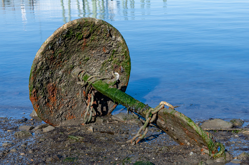 Close up view of a steel mushroom anchor or anchor block lying on the mudflat at the edge of a body of water