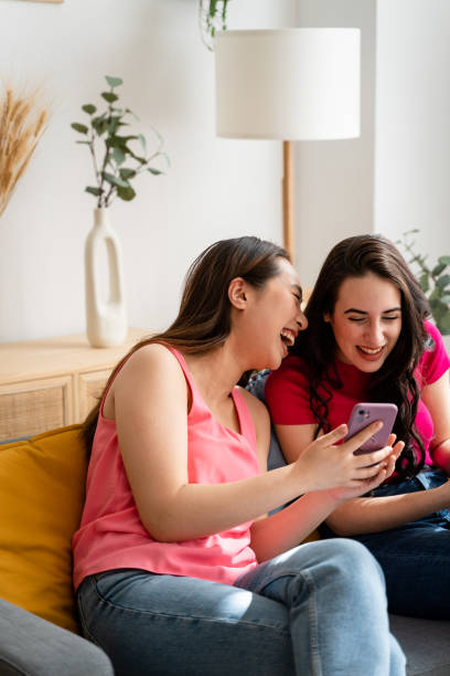 istock Smiling girlfriends using mobile phones at home. 1487464766
