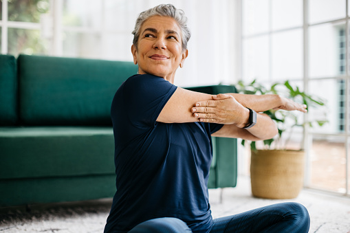 Happy and healthy senior woman doing a shoulder mobility exercise at home, working out with a cross arm stretch in her yoga session. This mature woman is keeping herself active with a fitness routine, maintaining physical wellbeing and wellness as she ages.