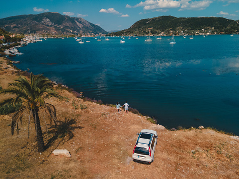overhead view of the couple standing near car looking at sea harbor with yachts and boats Lefkada island Greece