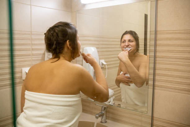 une jeune femme se brosse les dents dans une salle de bain. - toothbrush brushing teeth brushing dental hygiene photos et images de collection