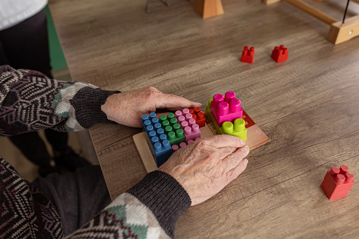 Senior man  with dementia is using block toy at his in-home therapy session.