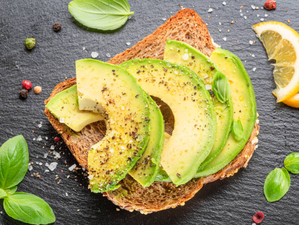 Avocado toast - bread with avocado slices on natural slate serving board. Top view.