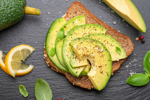istock Avocado toast - bread with avocado slices on natural slate serving board. Top view. 1487469726