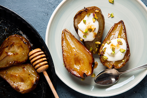 Baked pears with honey served with cream cheese and chopped pistachio in a blue dish