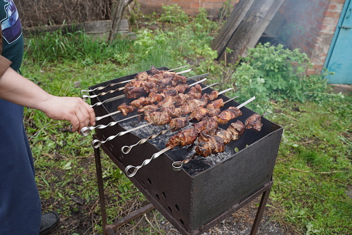 Shashlik - traditional Georgian barbecue. Closeup of raw roasted marinated meat barbecue shish kebab shashlik on steel metal skewers lying grill fire brazier with charcoal. Making barbecue.