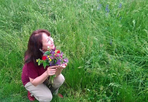Happy smiling middle age brunette woman sits with a bouquet of flowers plucked in a meadow.