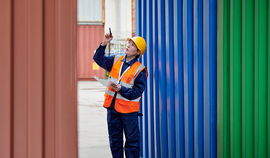 Side view of one asian females inspector examining and checklist cargo container data at loading dock.
