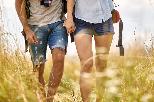 Close up shot of couple hiking in field,  holding hands. Nature outdoors. Caucasian couple. Sport, freedom, holiday concept.