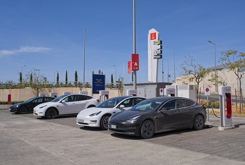 Loule, Portugal - April 11, 2023: A static shot of a solid black Tesla Model 3 dual motor charging at the Loule Supercharger in a sunny spring day. Selective focus.