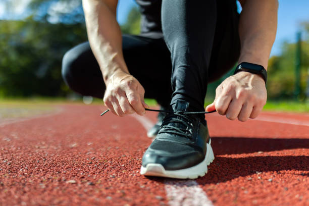 晴れた日にスポーツスタジアムで靴ひもを結ぶ男性の手、ランニングとトレーニングを開始する前のランナーの接写写真 - running jogging men shoe ストックフォトと画像