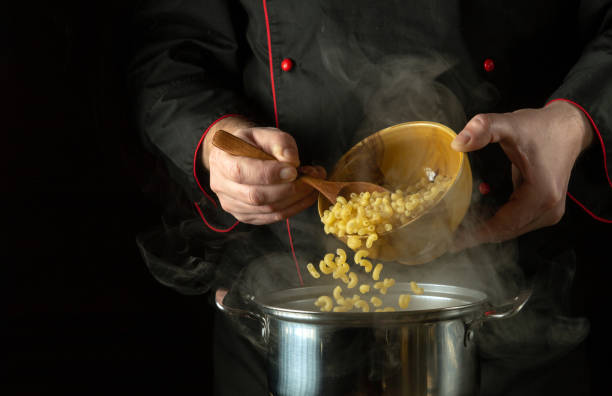 The cook spoons the pasta into the pan. Dark space for recipe or menu. The idea of cooking delicious pasta in the restaurant kitchen