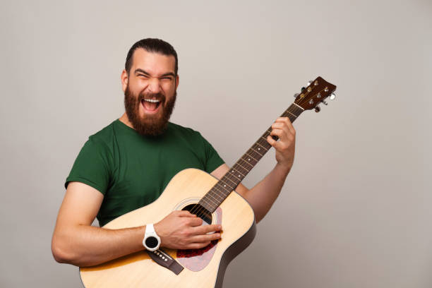 istock Ecstatic young bearded man is holding and playing rock on an acoustic guitar. 1487482756