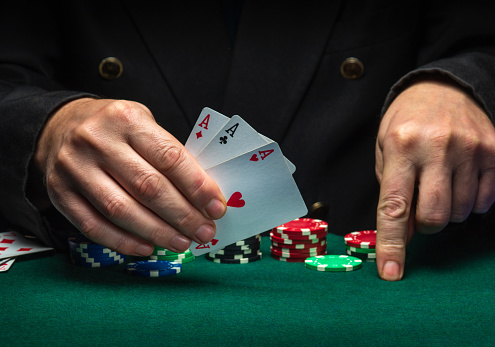The player shows playing cards with a winning combination of three of a kind or a set in a poker game on a green table with chips in a club.