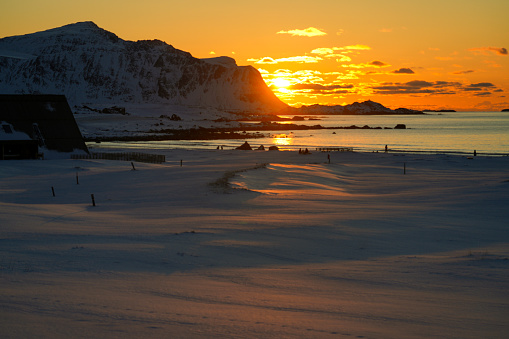 Evening sun getting down above the Lofoten Islands. In front is sun reflection on sea water and snow on the beach. Northern Norway.