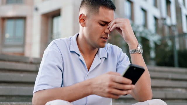 Phone, bad news or regret with a man in the city, sitting on steps while reading a negative text message. Sad, problem and 5g mobile technology with an unhappy young male feeling bad in an urban town
