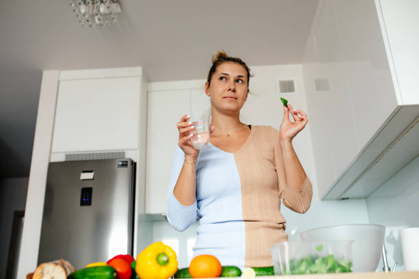 istock Charming hostess thoughtfully drinks water and tastes basil leaf, cooks dishes from various fresh vegetables at home. 1487490926