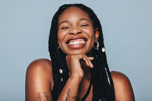Happy woman with face piercings smiling at the camera in a studio. Young black woman feeling confident in herself.
