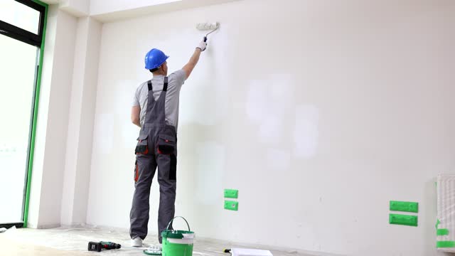 Foreman in uniform paints wall in white using roller