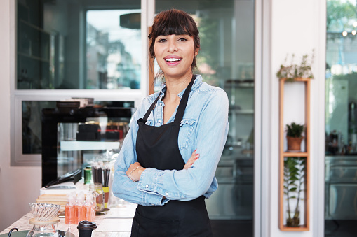 Caucasian Young barista woman is wearing apron standing and Smiling for happy at counter bar in cafe. Start up for Coffee shop and cafe business owner concept.